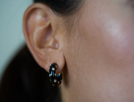 Gold-tone hoop earrings with black enamel and blue zirconia stones on hoop.