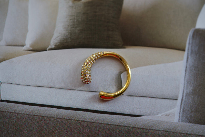Gold-tone C-shaped crystal ring with sparkling rhinestone inset across the curve