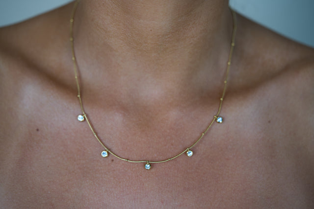 Gold charm drop necklace with small round blue stones on a delicate chain